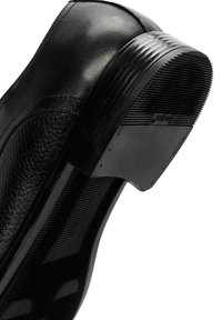 Chaussure noire en cuir avec une tige texturée, bout rond et semelle en caoutchouc rainurée. Talon plat notable avec un petit logo de la marque.