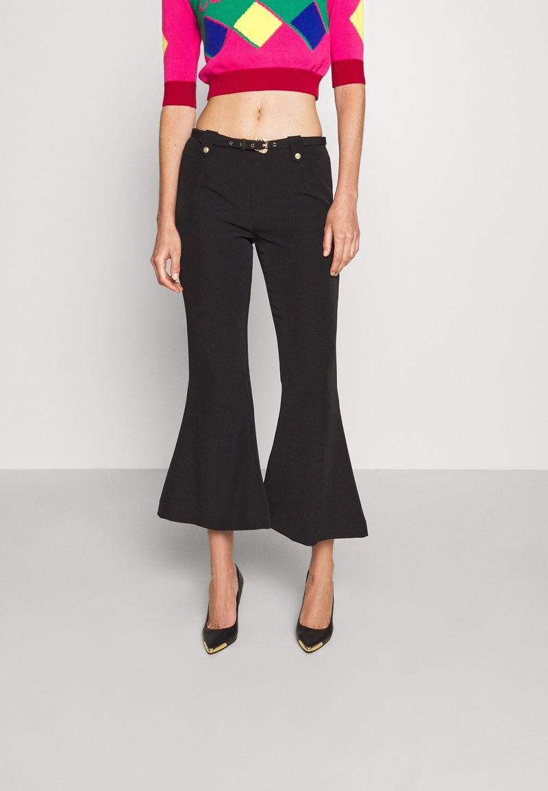 Pantalons évasés noirs avec une texture lisse, dotés d'une taille ajustée, d'accents de boutons en or et d'un top court avec un motif en diamants multicolores.
