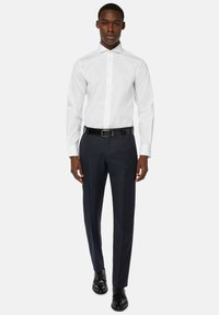 Bela srajca z uskim ovratnikom, v kombinaciji s temno modrimi hlačami in črnim pasom. Obleka ima prilagojen kroj in gladko tkanino.