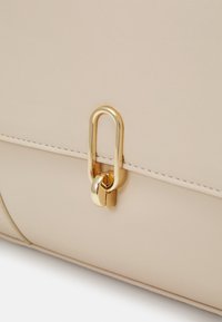 Beige Ledertasche mit einem goldfarbenen Metallverschluss und einer glatten Textur, mit Ziernähten entlang des Randes.