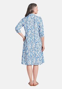 Blau-weiß gemustertes Kleid mit Dreiviertelärmeln, knielangem Saum und lockerer Passform. Glattes Material, abstraktes Blumen- und geometrisches Design.