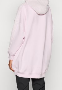 Felpa oversized in tessuto rosa chiaro con cappuccio e maniche testurizzati e pelosi. Presenta fessure laterali all'orlo e polsini a coste.