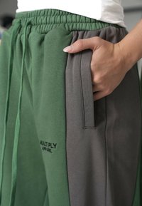 Pantaloni joggers verzi și gri cu un talie elastică, buzunare laterale și detalii cusute. Logo-ul "MULTIPLY APPAREL" vizibil pe față.