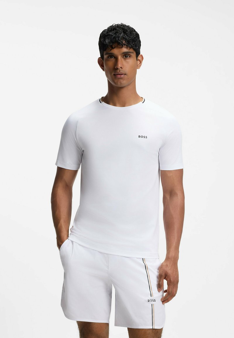Homme portant une chemise blanche à manches courtes et un short assorti avec le logo « BOSS » et de fines rayures verticales sur le short.