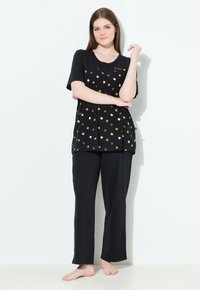 Conjunto de pijama negro que incluye una camiseta de manga corta con un patrón floral en blanco, amarillo y marrón, combinada con pantalones negros holgados.
