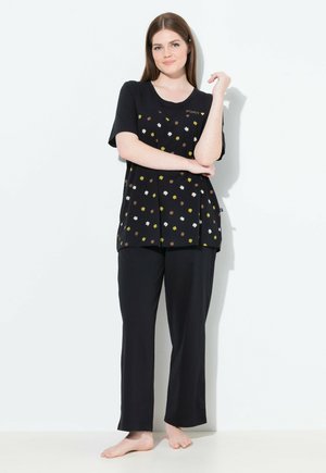 Zwart pyjama-set met een korte mouwen top met een bloemenpatroon in wit, geel en bruin, gecombineerd met losse zwarte broek.
