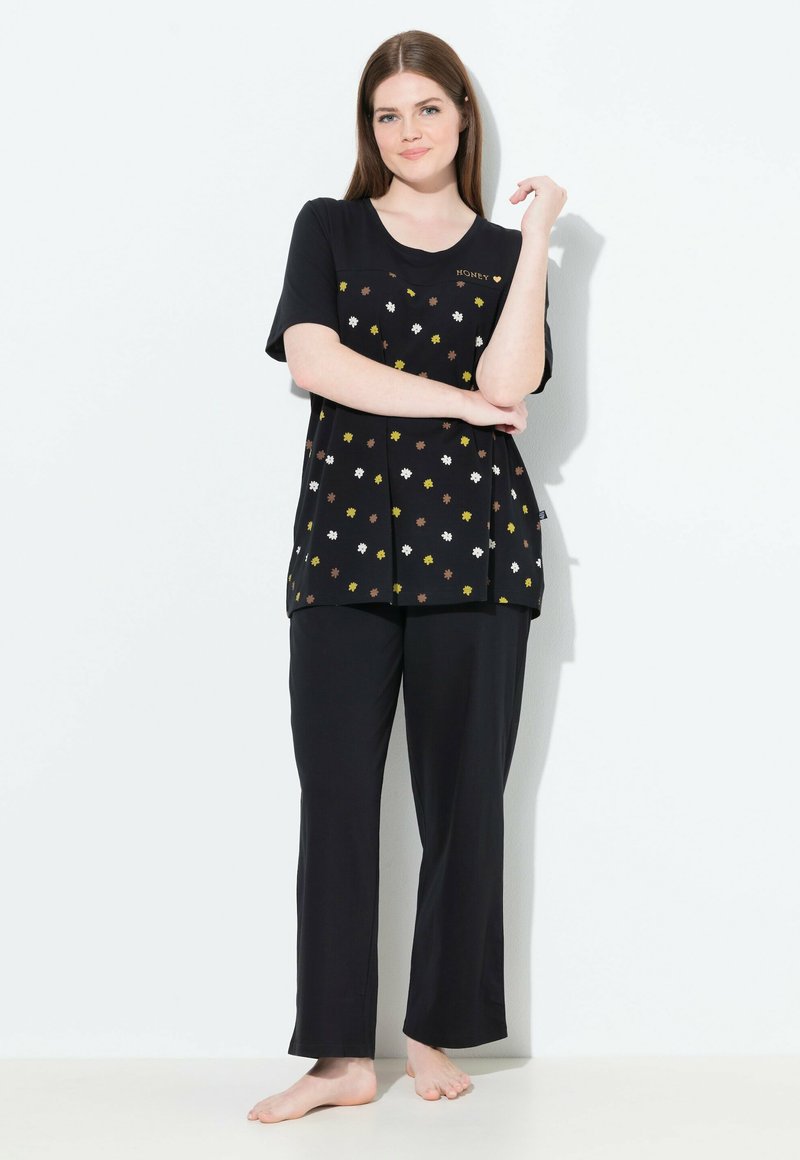 Conjunto de pijama negro que incluye una camiseta de manga corta con un patrón floral en blanco, amarillo y marrón, combinada con pantalones negros holgados.