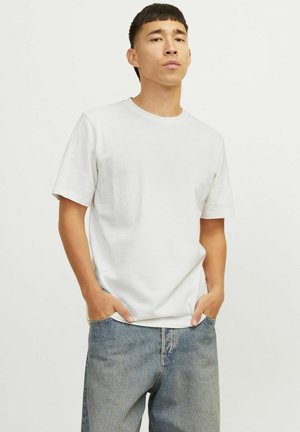 Kortærmet t-shirt med rund hals i hvid, lavet af tekstureret stof, parret med løse blå denimjeans. Hænderne i lommerne.