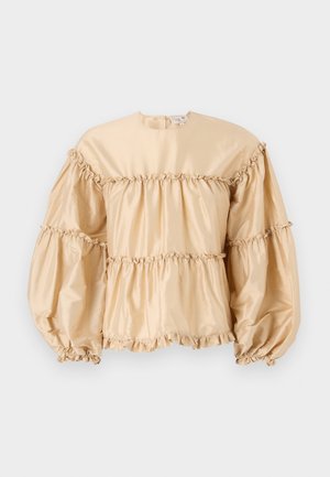 Beigā satīna blūze ar pūkām, kārtaina dizaina un sasietiem detaļām gar šuvēm. Apaļa dekoltē ar aizmugurējo aizdari.