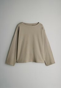 Ilgi piedurkņu, apaļas kakla tops, izgatavots no maigas, gaiši bēšas auduma. Tam ir brīva piegriezuma forma un nokritušas plecu šuves, kā arī minimālas šūšanas detaļas.