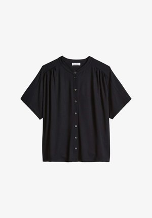 Zwarte blouse met korte mouwen, ronde hals, een knoopsluiting aan de voorkant en subtiele plooien op de schouders.