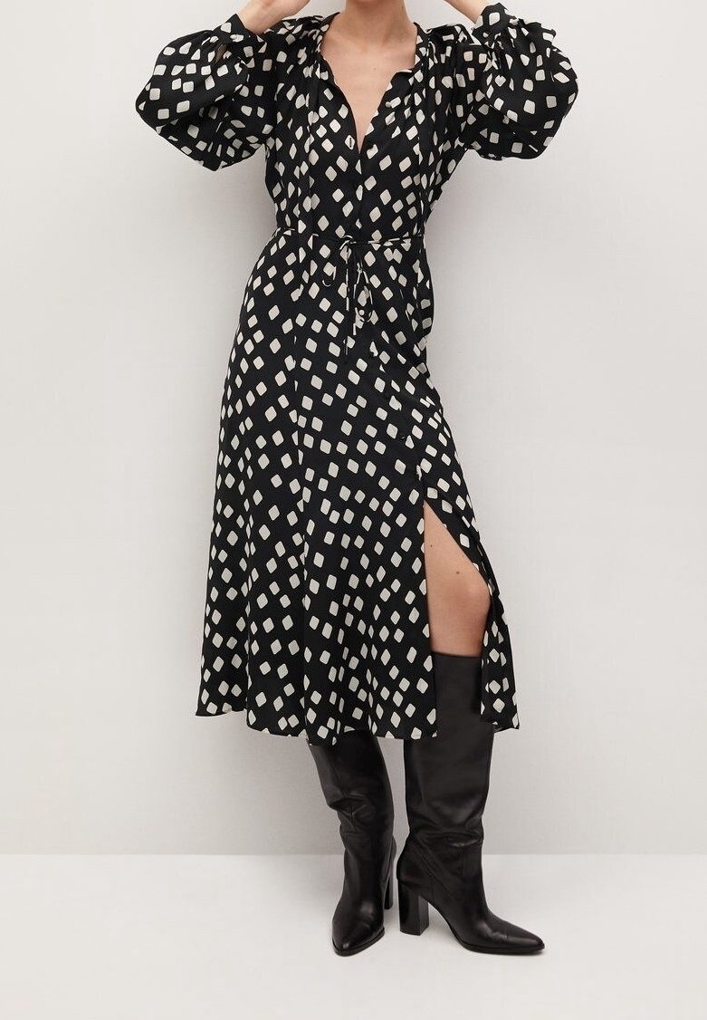 Vestido negro ajustado con un patrón geométrico blanco, mangas largas abullonadas, una abertura en la parte delantera y combinado con botas de tacón negras hasta la rodilla.
