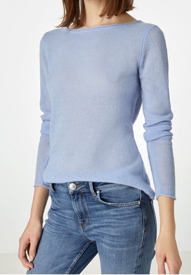 Femme portant un pull bleu clair à manches longues et un jean bleu moyen, debout avec les mains relâchées le long du corps.
