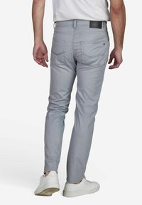 Pantalon gris clair avec une coupe slim, fabriqué dans un tissu lisse, avec des poches arrière et une patch logo en cuir noir sur la taille.