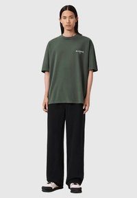 Tume-roheline puuvillane üle suuruses T-särk lühikeste varrukatega ja valge logoga. Ühildatud lapsele lahtiste mustade pükste ja must-valgete tossudega.