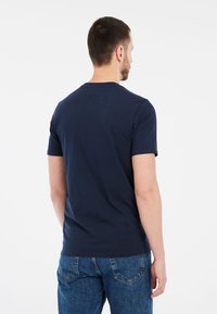 Námornícky modré tričko s krátkym rukávom, vyrobené z bavlny, s okrúhlym výstrihom a voľným strihom, v kombinácii s svetlomodrými džínsami.