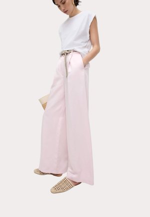 Wit mouwloos topje gecombineerd met hooggetailleerde, wijde roze broek met een gevlochten riem, aangevuld met geweven instapschoenen.