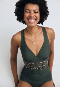 Maillot de bain une pièce vert avec un décolleté en V profond et une bande décorative imprimée léopard autour de la taille. Matière lisse et design ajusté.