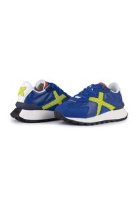 Sneaker blu con accentuazioni in rete gialla, tallone bianco e suola in gomma nera. Presenta una tomaia testurizzata e colori a contrasto nel design.