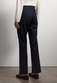 Pantalones de mezclilla oscura con corte recto, cintura alta y textura sutil. Presentan un dobladillo limpio y un detalle mínimo en los bolsillos traseros.