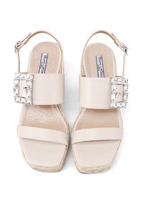 Sandali espadrilles beige con una larga fascia, una fibbia decorativa in cristallo trasparente e una soletta testurizzata, caratterizzati da un tallone aperto e una suola piatta.
