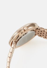 Reloj de oro rosa con caja de metal pulido, bisel texturizado y diseño de pulsera de eslabones; cuenta con un botón lateral y un fondo de cristal reflectante.