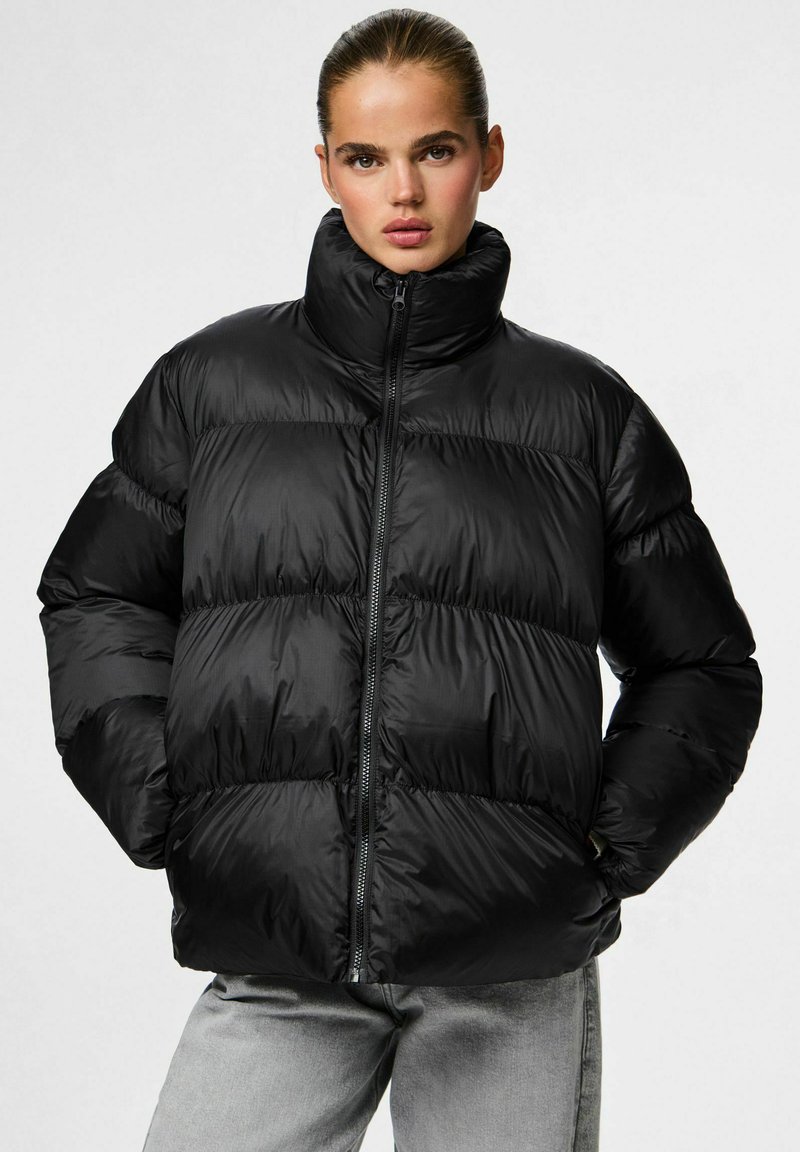 Chaqueta aislante negra con cuello alto, fabricada en un material brillante, con diseño acolchado, cremallera frontal y puños elásticos.