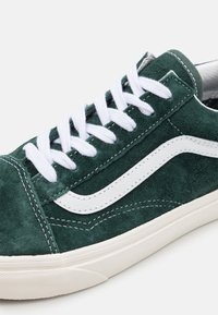 Baskets en daim vert avec des accents blancs, des lacets plats blancs, une surface texturée et une semelle en caoutchouc vulcanisé avec des coutures décoratives.