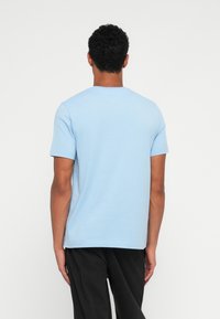 Ανοιχτό μπλε βαμβακερό μπλουζάκι με στρογγυλή λαιμόκοψη και κοντά μανίκια, εμφανιζόμενο από την πίσω πλευρά. Έχει λείο ύφασμα και άνετη εφαρμογή.