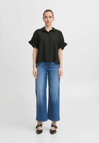 Black short-sleeve button-up shirt with ruffled cuffs, paired with wide-leg blue jeans and black heeled sandals. Simple and casual design.