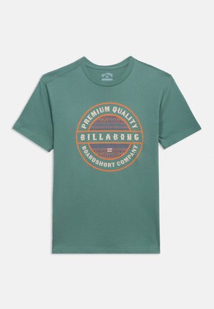 Roheline lühikeste varrukatega ümmarguse kaelusega t-särk, millel on oranži ja lilla ringikujuline logo, millel on kiri „Premium Quality Billabong Boardshort Company“.