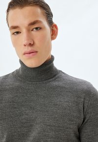 Grå turtleneck-tröja i mjukt tyg, med en figursydd design och ribbad krage, samt en jämn och slät yta.