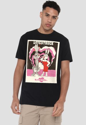 Young man wearing black T-shirt with cartoon rabbits, one in red dress, surrounded by pink hearts, text "Lovestruck" and "My love machine."