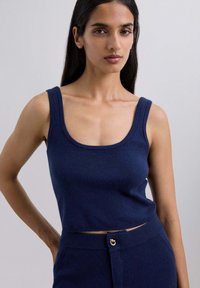 Top sin mangas en azul marino con escote en forma de pala y bordes acanalados. El material parece suave. Combinado con pantalones de tiro alto a juego.