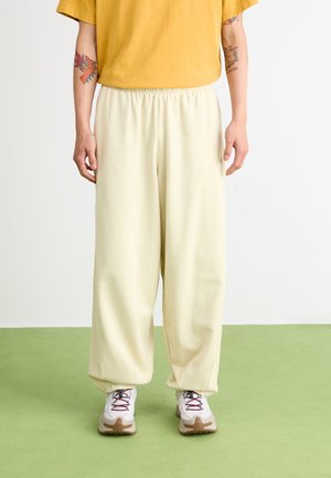 Chemise jaune, pantalon crème ample avec ceinture élastique et baskets blanches avec accents rouges. Surface plate et texturée en dessous.