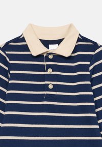 Polo-shirt à manches longues bleu marine et beige à rayures, avec un col beige et trois boutons beiges sur la patte de boutonnage avant.