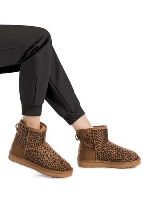 Botas de tobillo de estampado de leopardo en ante marrón con una superficie texturizada, un interior suave y una suela de goma. Combinadas con pantalones negros ajustados.
