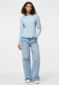 Maglietta a maniche lunghe azzurro chiaro con motivo floreale e orlo scallop, abbinata a jeans a gamba larga azzurro chiaro e sneakers bianche.