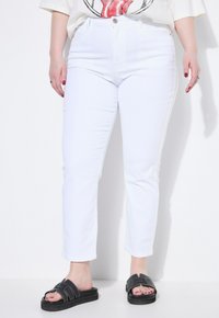 Vita högmidjade jeans med smal passform och lätt ankellängd, i kombination med svarta slidesandaler med sömda detaljer.