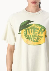 Camiseta de algodón de corte relajado en color crema, con un audaz gráfico de limón amarillo acompañado de hojas verdes y el texto "BITTER SWEET" en una tipografía estilizada.