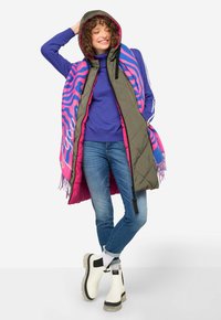 Vadderad olivgrön väst med huva, rosa innerfoder och en livlig nyckelblå och rosa mönstrad scarf. Bärs med jeans i denim och vita stövlar.