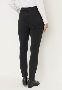 Musta, kapealinjaiset farkut, joissa on korkea vyötärö ja kaksi takataskua. Materiaali näyttää olevan joustavaa. Yhdistetty mustiin nilkkureihin.