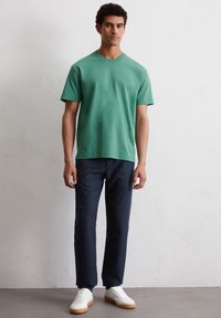 Groene katoen t-shirt met korte mouwen, gecombineerd met marineblauwe broek en witte sneakers. Soepele textuur, klassieke pasvorm en minimalistisch design.