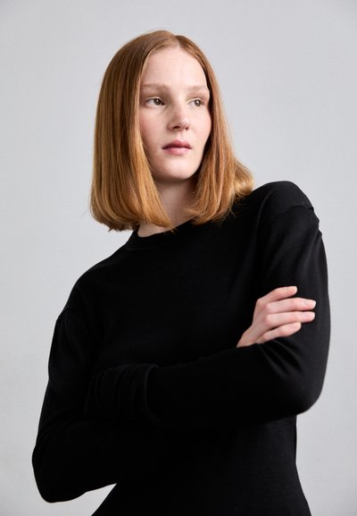 Top nero a maniche lunghe con scollatura rotonda. Realizzato in un tessuto morbido e leggero. Presenta maniche aderenti e una silhouette affusolata.