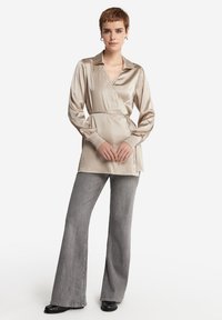 Satinwrapskjorta i ljusbeige med krage, långa ärmar och knytmidja. I kombination med grå utsvängda jeans och svarta skor.