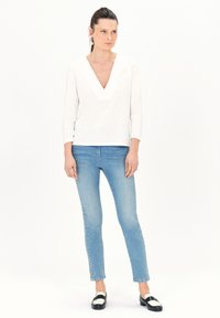 Witte lange mouwen top met een V-hals en subtiele ontwerpen, gecombineerd met lichtblauwe slim-fit jeans en zwart-witte instappers.