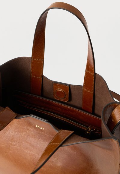 Καφέ δερμάτινη τσάντα τύπου tote με ομαλή και υφασμένη επιφάνεια, διαθέτει δύο μακριές λαβές και εσωτερική τσέπη με φερμουάρ. Λογότυπο ανάγλυφο στο εσωτερικό.