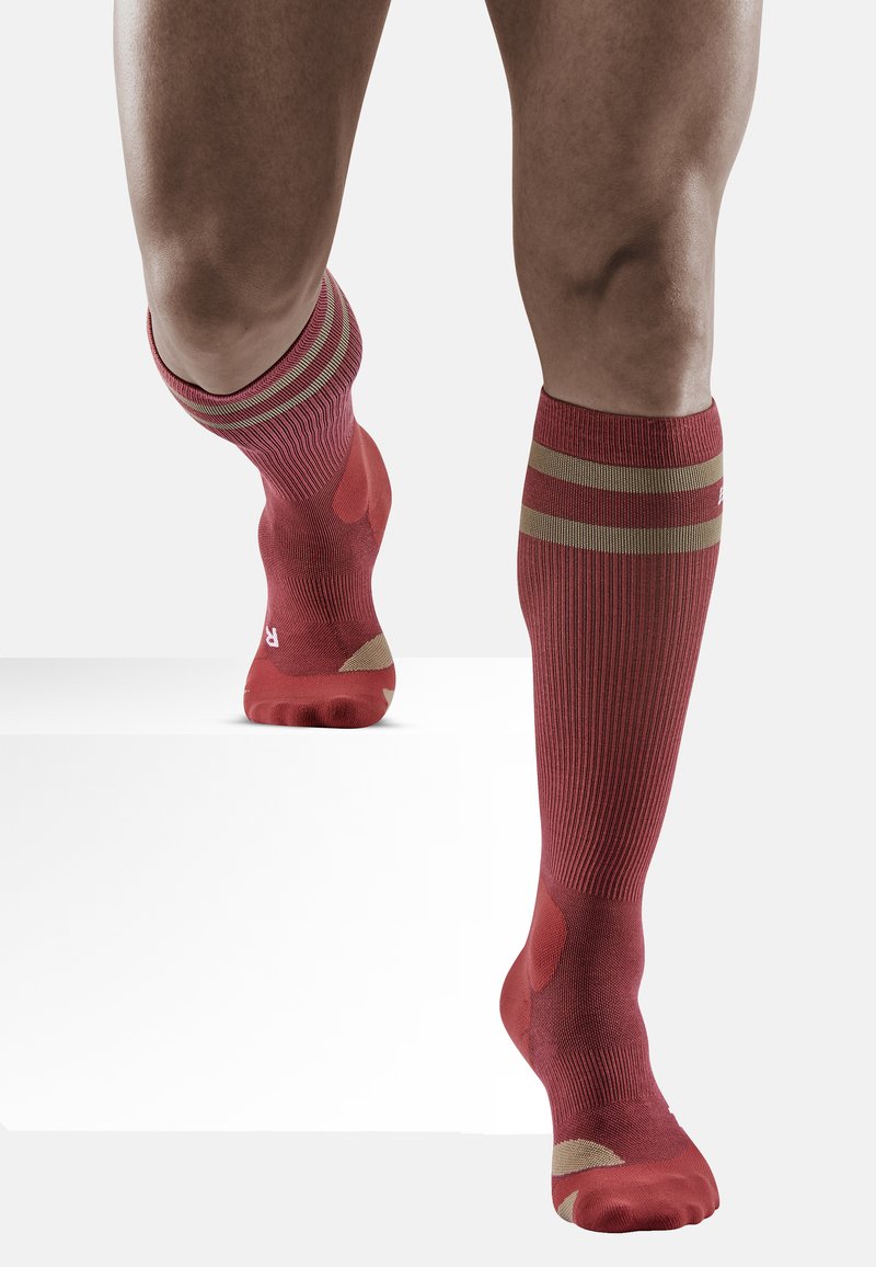 Rote kniebedeckende Socken mit geripptem Design, zwei horizontalen goldenen Streifen oben und verstärkten Zehen- und Fersenbereichen für Haltbarkeit.