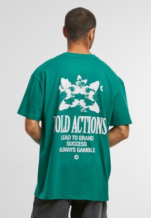 T-shirt vert en coton à la coupe décontractée, présentant un graphique de papillon blanc et un texte audacieux au dos. Manches courtes, design col rond.