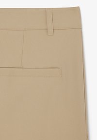 Nahaufnahme beiger Hose, die den Bund, die Gürtelschlaufe und die horizontale Gesäßtasche mit feinen Nähten zeigt.